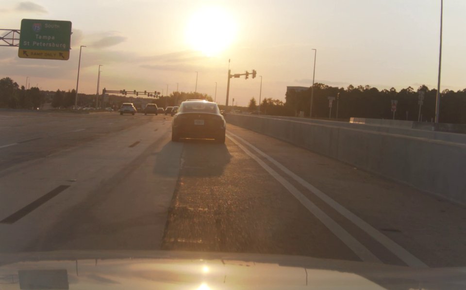 Forward camera frame on a Tampa interstate at sunset, with sun glare washing out the lane lines