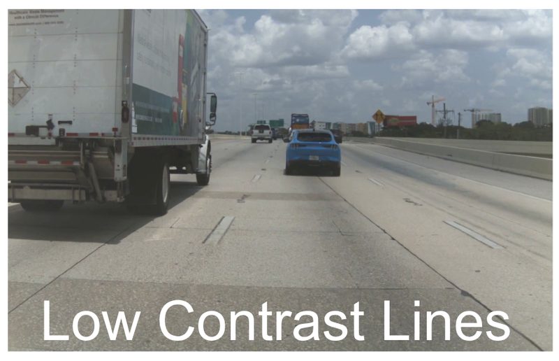 White lane lines on pale concrete beside a truck; the lines barely stand out from the pavement